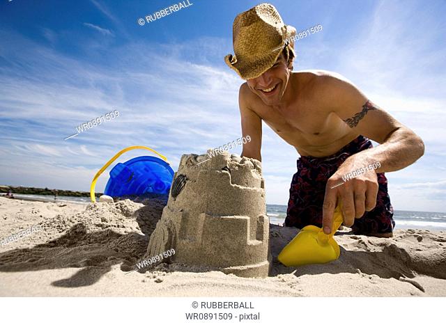 Low angle view of a young man digging sand on the beach