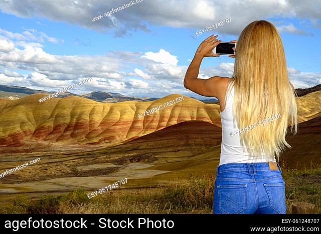 Casual young nature lover woman using her mobile phone to take photos of the Painted Hills Unit - John Day Fossil Beds National Monument, Oregon, USA