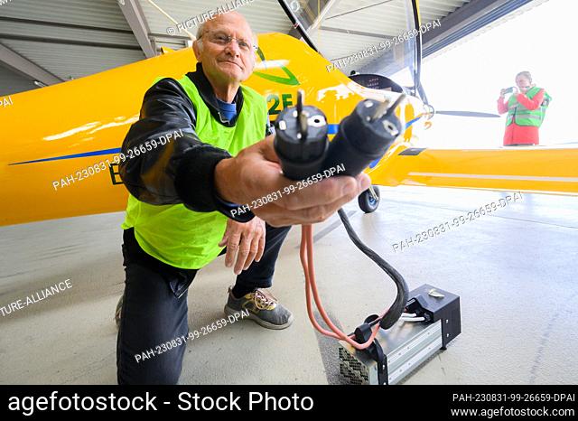 31 August 2023, Lower Saxony, Hanover: Test pilot Uwe Nortmann shows a voltage converter in front of the ""Elektra Trainer"" e-airplane at Hannover Airport