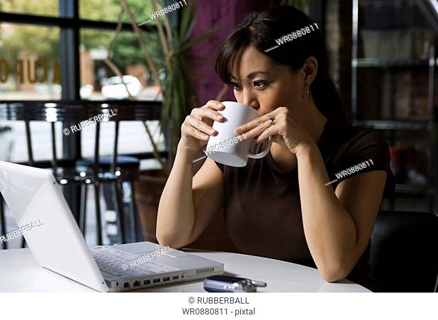 Young woman drinking coffee and working on a laptop