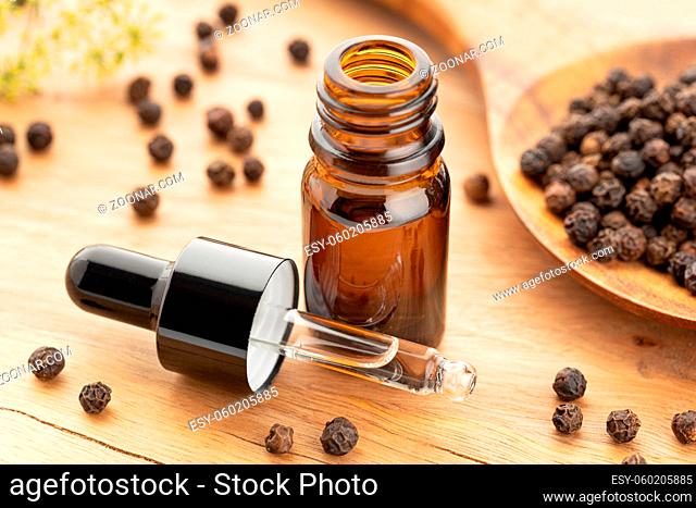 Black pepper essential oil on bottle on wooden table. Peppercorn oil Alternative medicine