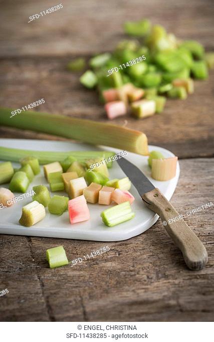 Peeled and chopped rhubarb on a ceramic board with a kitchen knife