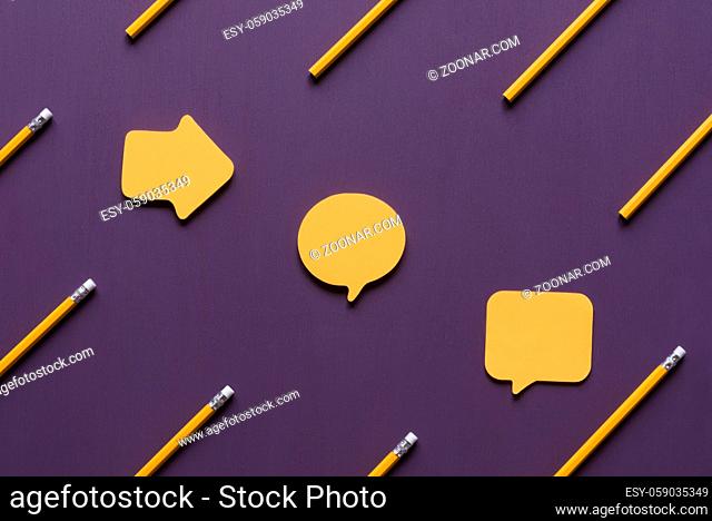 Unwritten yellow post-it notes in different shapes placed on a purple wooden background, surrounded by yellow wooden pencils