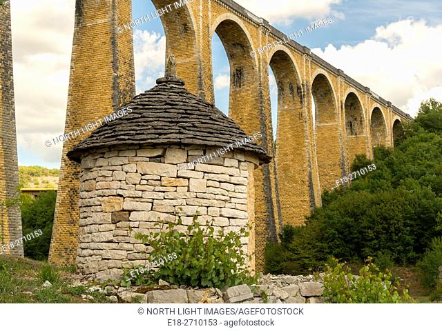 France, Midi-Pyrénées, Lot, Souillac. High arching, stone supports of railway bridge over deep valley. Old stone shed in the foreground