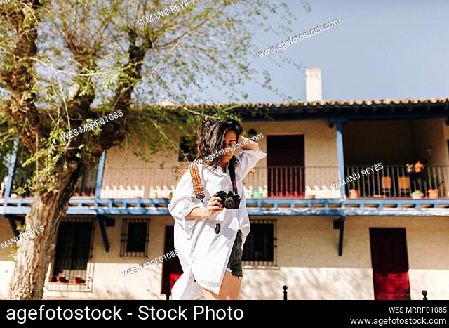 Woman with hand in hair holding camera at village