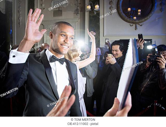 Well dressed male celebrity waving to fans and paparazzi at red carpet event