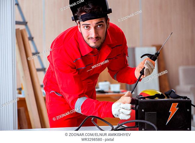 Young repairman with a welding gun electrode and a helmet welding metal