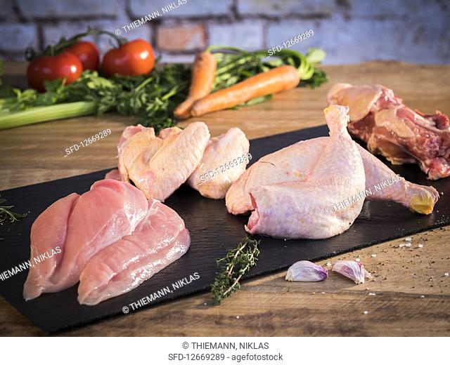 Fresh chicken, divided into breasts, drumsticks, wings and carcasses, with soup vegetables behind