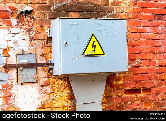 Old yellow high voltage warning sign hanging on the metall box with electrical equipment