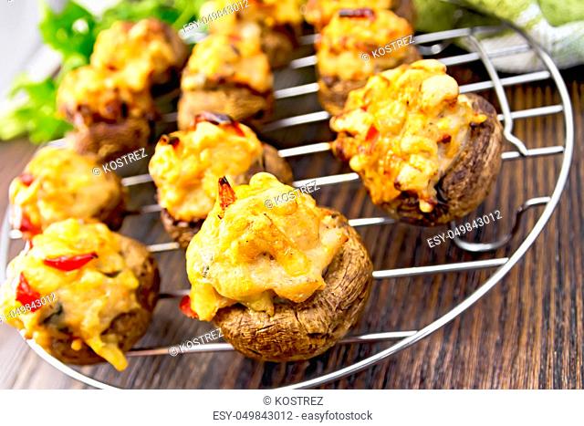 Mushrooms stuffed with meat and pepper on a metal grid on the background of wooden boards
