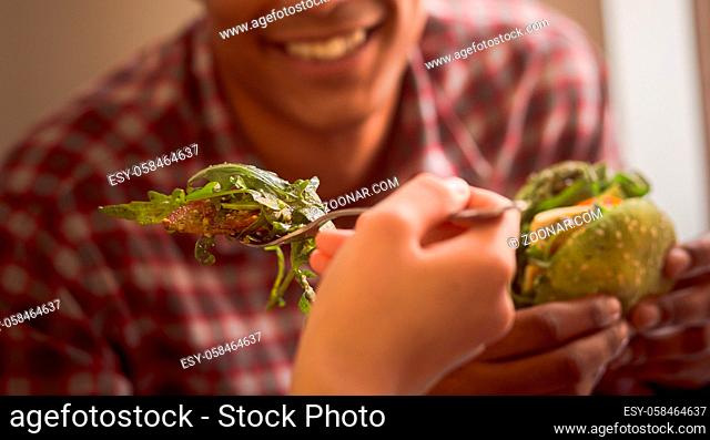 Happy couple spending free time in vegan restaurant or cafe. Closeup picture of lady feeding her boy-friend with vegan salad