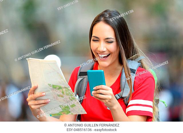 Happy teen tourist laughing using smart phone and holding a paper map on the street