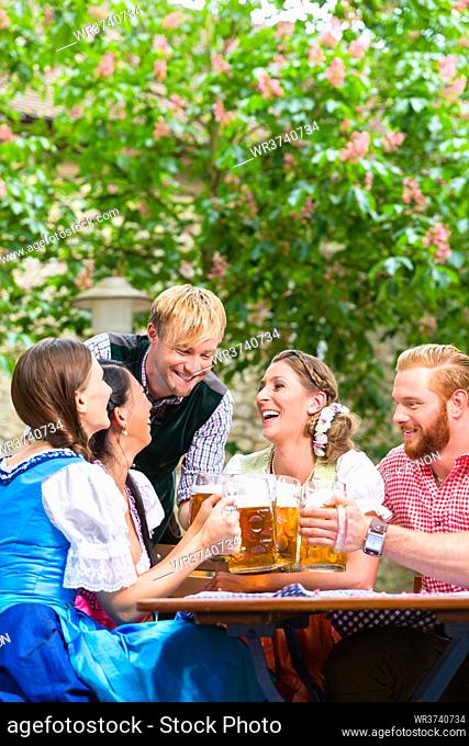 ive friends in Bavarian clothes clinking beer glasses in beer garden