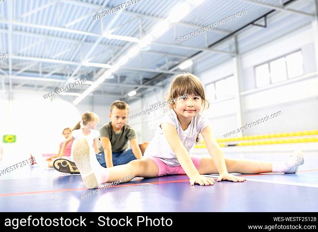Girl practicing splits sitting with friends at school sports court