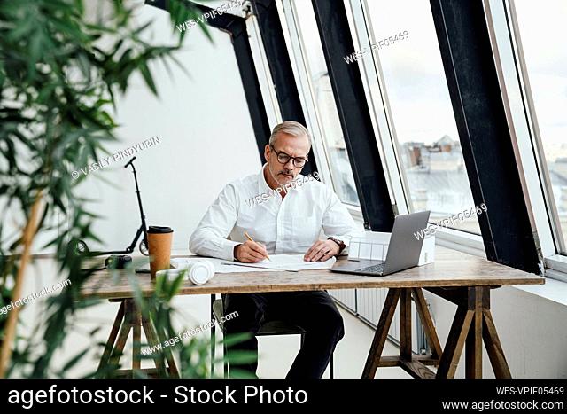 Businessman writing on document by laptop in office