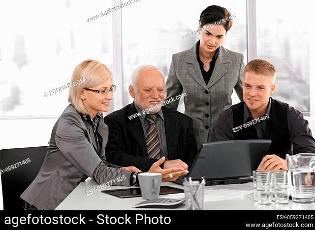 Businessteam working together, mid adult businesswoman showing project on computer to senior executive, colleagues watching