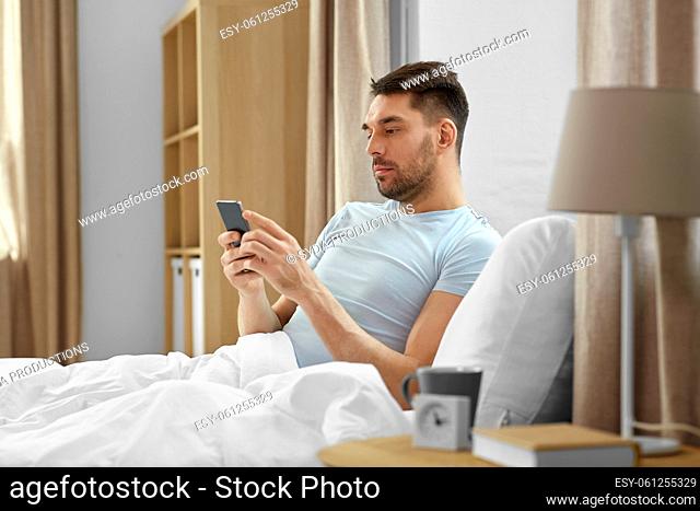 man with smartphone in bed in morning at home