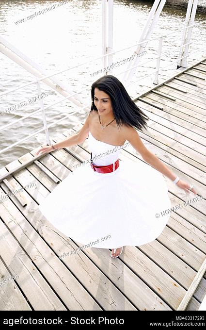 Young woman with white dress is dancing on a bridge