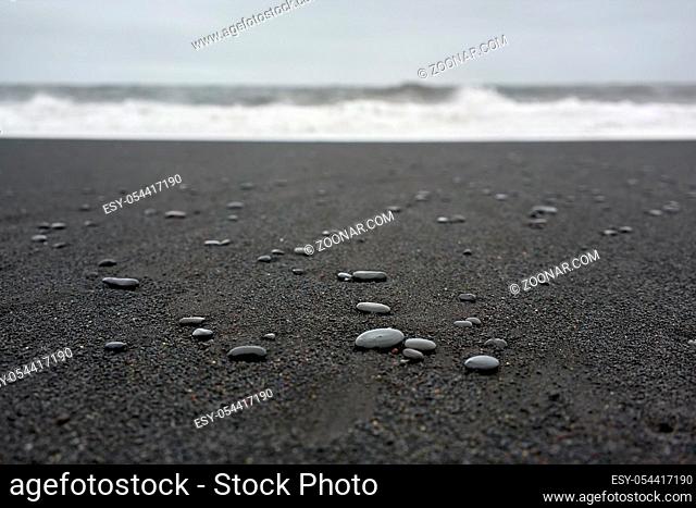 Pebbles on the black sand beach on the background of the stormy sea in Iceland. Closeup. Horizontal