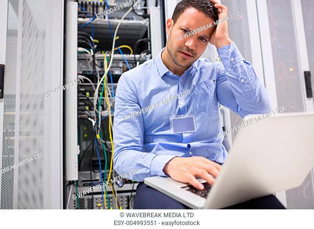 Technician getting frustrated with laptop over servers in data center
