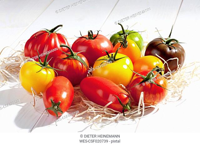 Different tomatoes on wood wool and wooden table