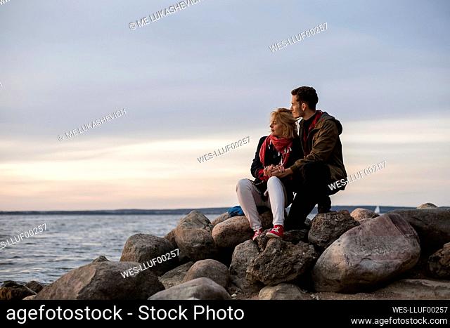 Couple looking at sea while sitting on rock