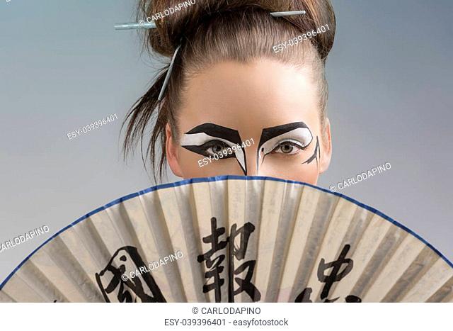 sexy brunette with japan make-up and asian fan, she takes the fan on the face and her mouth and her nose are hidden