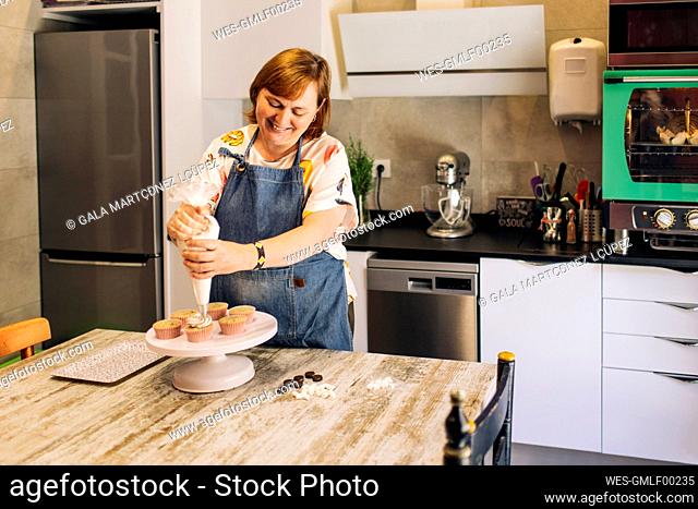Smiling mature woman icing cupcakes on cakestand in workshop