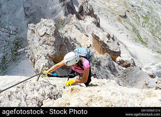 Horizontal view of a pretty female climber in lilac shirt on a steep Via Ferrata in the italian Dolomites with a great view behind