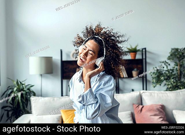 Young woman wearing headphones listening to music and dancing at home