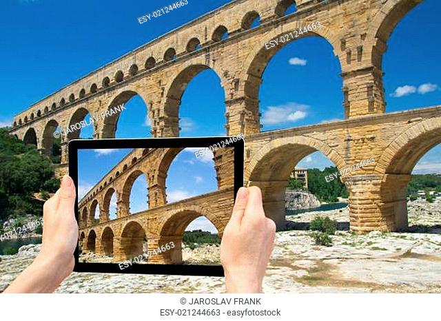 In the bottom left of the photo are hands holding tablet, whose screen contains photo of the Pont du Gard.  Background of the photo contains the same photo of...