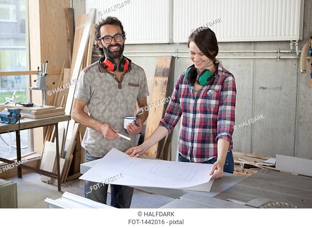 Laughing male and female carpenters with blueprint in workshop