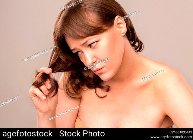 Gorgeous woman standing half turn and touching her hair. Looking at it with disappointment. Mid age woman over 35 years old concept