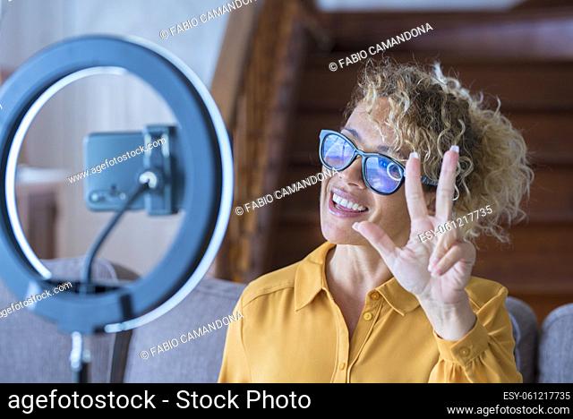Portrait of beautiful adult woman speaking in front of a phone to record online content - concept of modern home work and digital creator - video call...