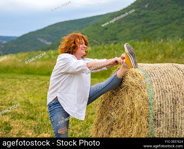 Mature woman raised leg high on haystack tying laces smiling looking away