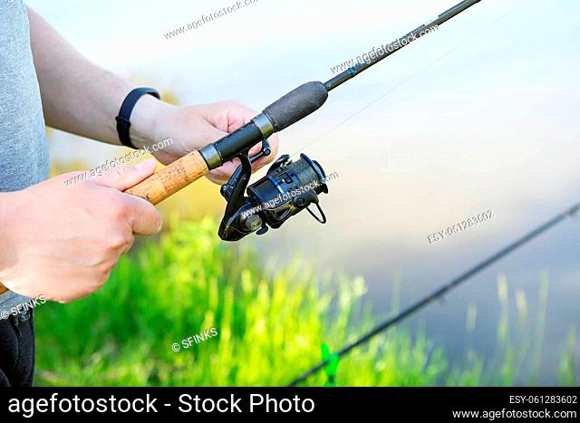 A fishing rod with a spinning reel in the hands of a fisherman. Fishing background. Outdoor recreation