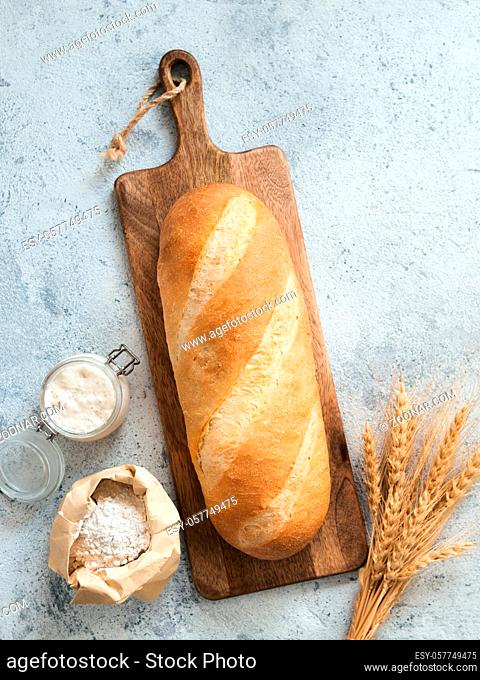 British White Bloomer or European sourdough Baton loaf bread on gray cement background. Fresh loaf bread, glass jar with sourdough starter