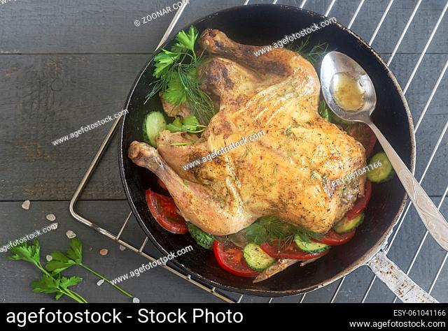 Fried chicken with cucumbers, tomatoes and parsley is on the table in a cast-iron frying pan. Top view, close-up