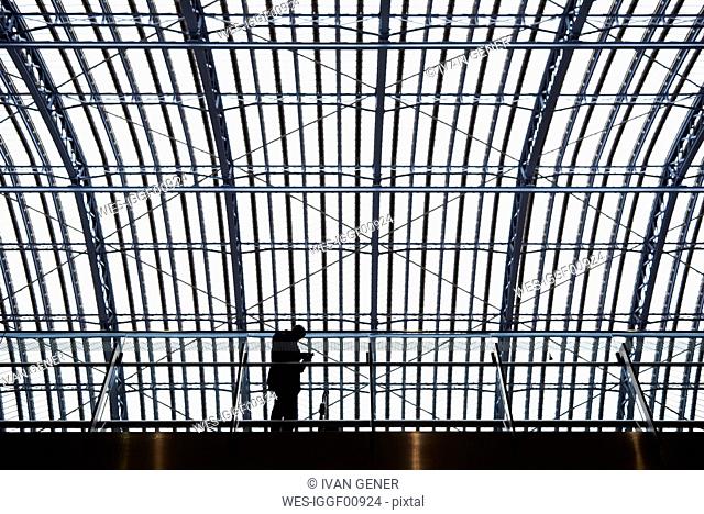 Silhouette of businessman standing on platform in train staion using mobile phone