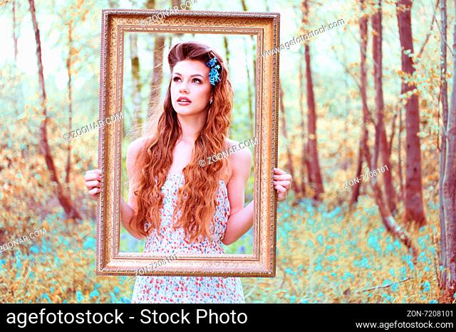Ravishing beautiful redhead long haired woman wearing a low-cut sleeveless dress with floral pattern while looking at camera through a brown handheld portrait...