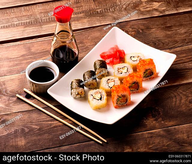 Sushi rolls with chopsticks and soy sause on black wooden table
