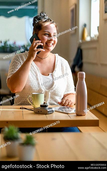 Voluptuous young woman talking over mobile phone while sitting at table in restaurant