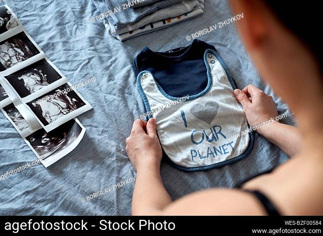 Pregnant woman folding baby clothes by ultrasound on bed at home