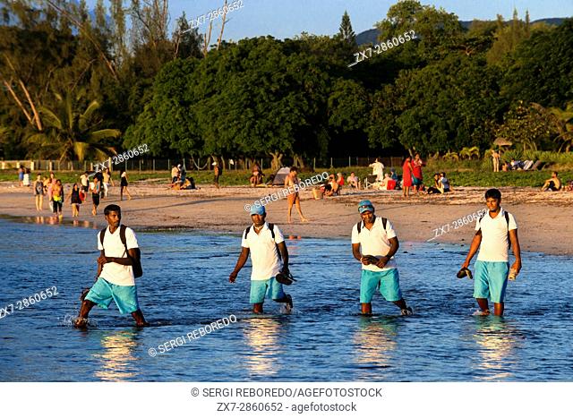 Hotel workers walking in Tamarin beach, Mauritius. Relection in the water