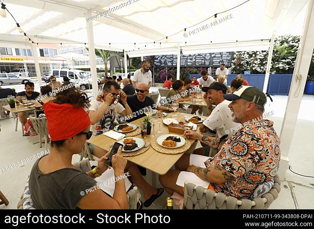 11 July 2021, Spain, Muro: A group of tourists eat in the restaurant Can Pescador on the beach Playa de Muro in the north of Mallorca