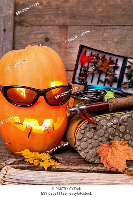 halloween pumpkin head with wading boots and fly-fishing tackles on wooden boards background