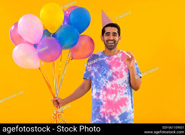 Portrait of happy young man holding balloons and party horn in hands