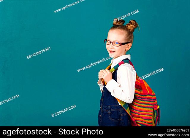 Funny little girl with big backpack jumping and having fun against turquoise wall. School concept. Back to School. School's out for summer
