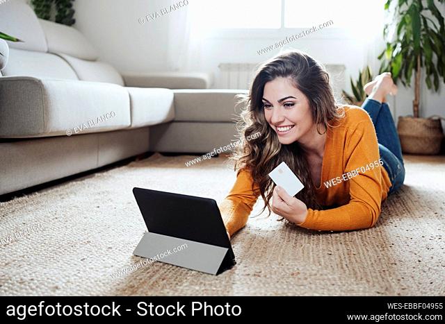 Happy woman doing home shopping through credit card and tablet PC