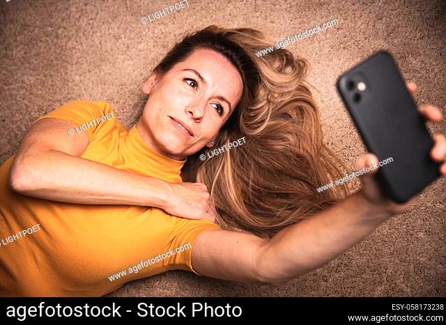 Happy mid-aged woman taking selfie with her smart phone at home